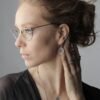 Stylish portrait of a woman wearing glasses and elegant jewelry, exuding sophistication.